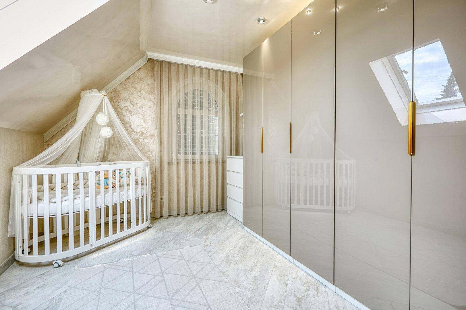 Helles Kinderzimmer im Dachgeschoss mit Babybett, Einbauschränken und Dachfenster, sehr gemütlich.