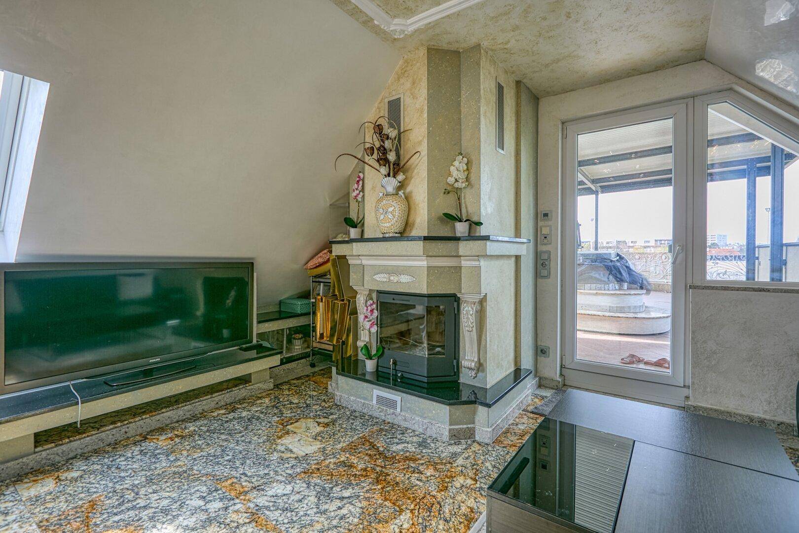 Gemütliches Wohnzimmer im Dachgeschoss mit Kamin, Fernseher und Zugang zur Dachterrasse.