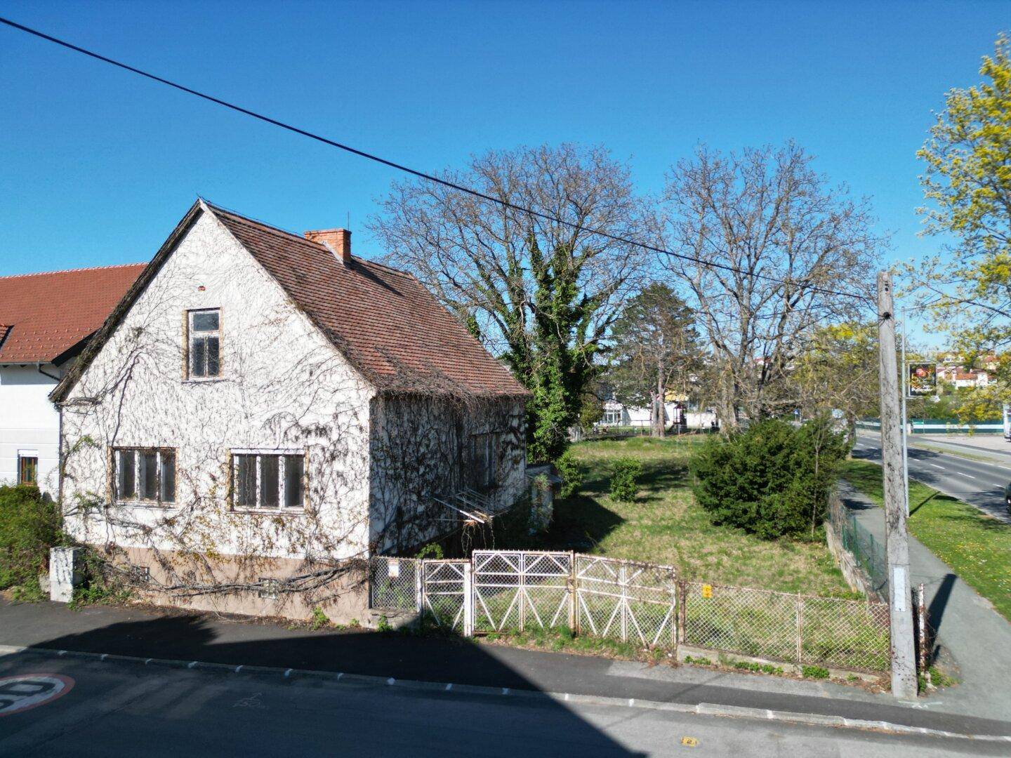 Älteres Haus mit Ziegeldach und kahlen Ranken an der Fassade, umgeben von einem Grundstück.