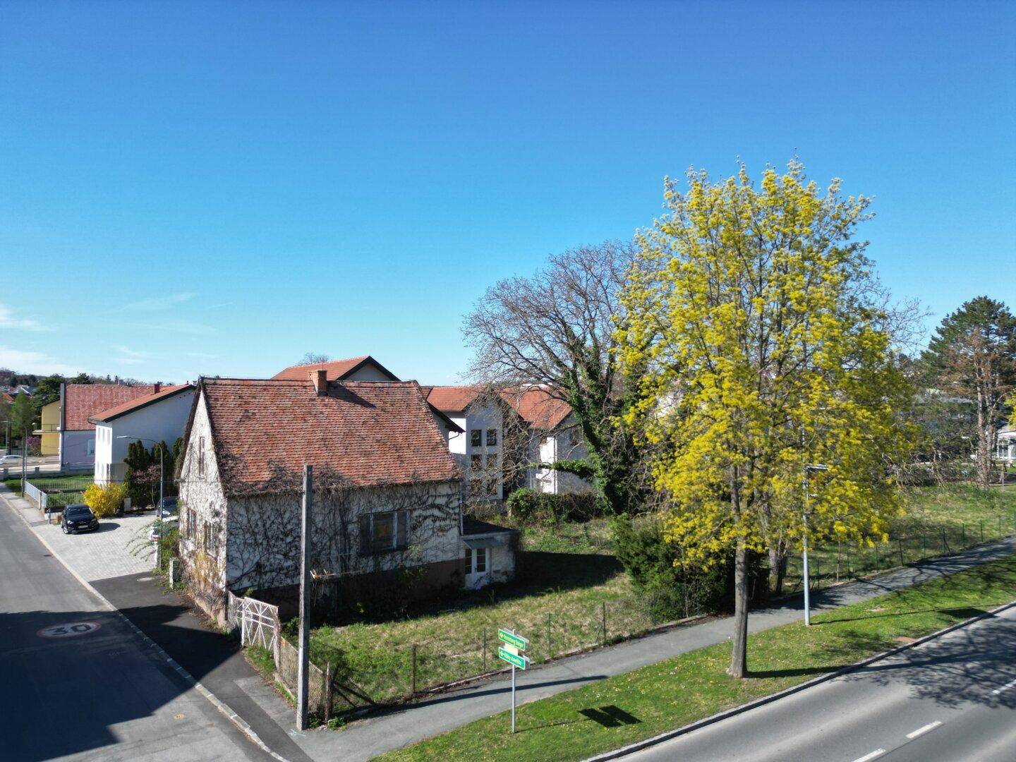 Luftaufnahme eines älteren Hauses mit Ziegeldach und umliegendem Grundstück an einer Straße.