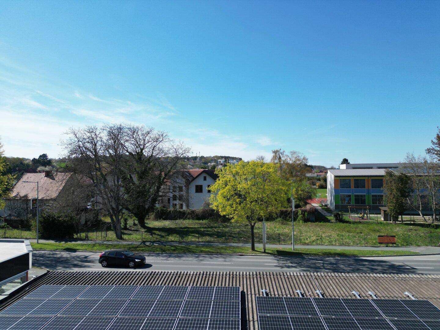 Weitläufige Ansicht des Grundstücks mit Bäumen und einem Auto auf der Straße, im Vordergrund Solarpaneele.