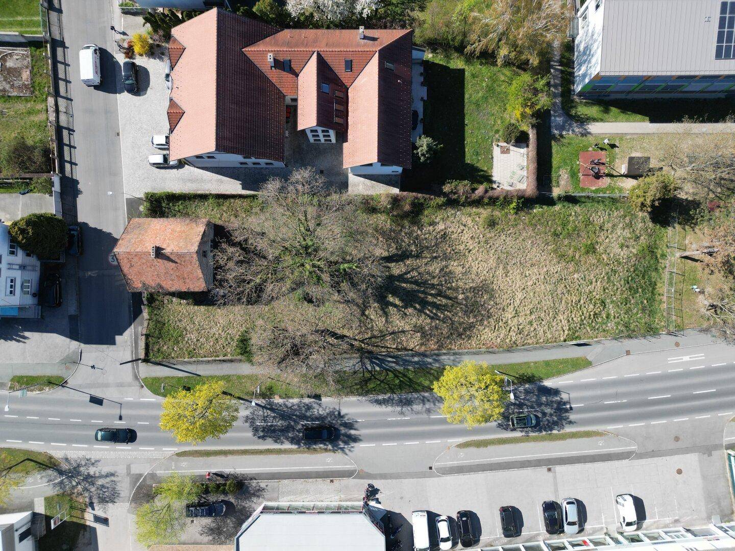 Luftaufnahme des Grundstücks mit Hauptgebäude, kleinem Haus, Bäumen und angrenzenden Straßen.