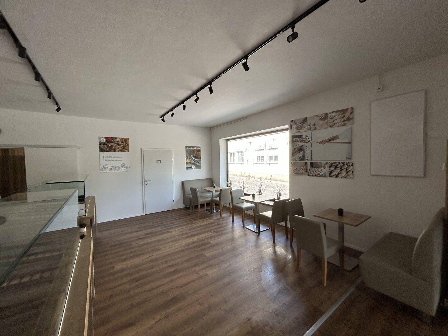 Heller Sitzbereich in einem Verkaufsraum mit Tischen, Stühlen und großen Fenstern.