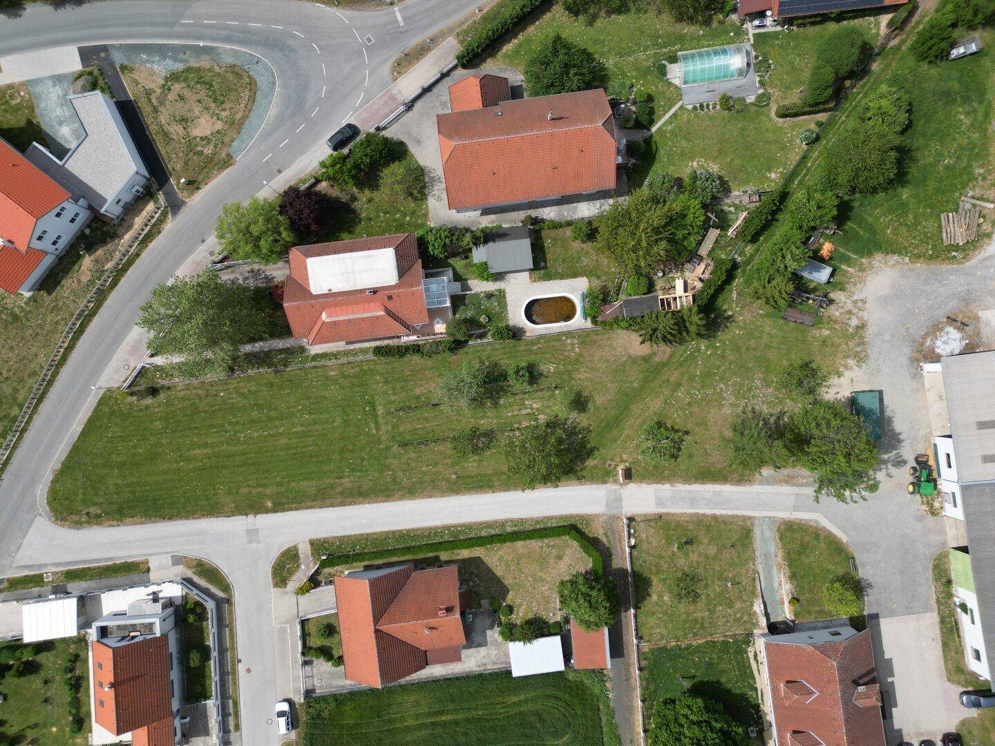 Luftaufnahme eines Wohngebiets mit mehreren Grundstücken, Häusern und einem Pool in der Nachbarschaft.