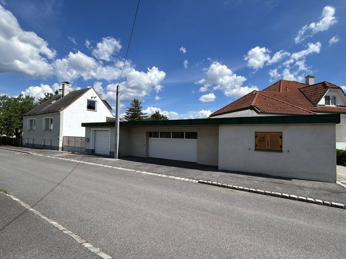 Straßenansicht des Anwesens mit zwei Garagen und einem weiteren Gebäude im Hintergrund.