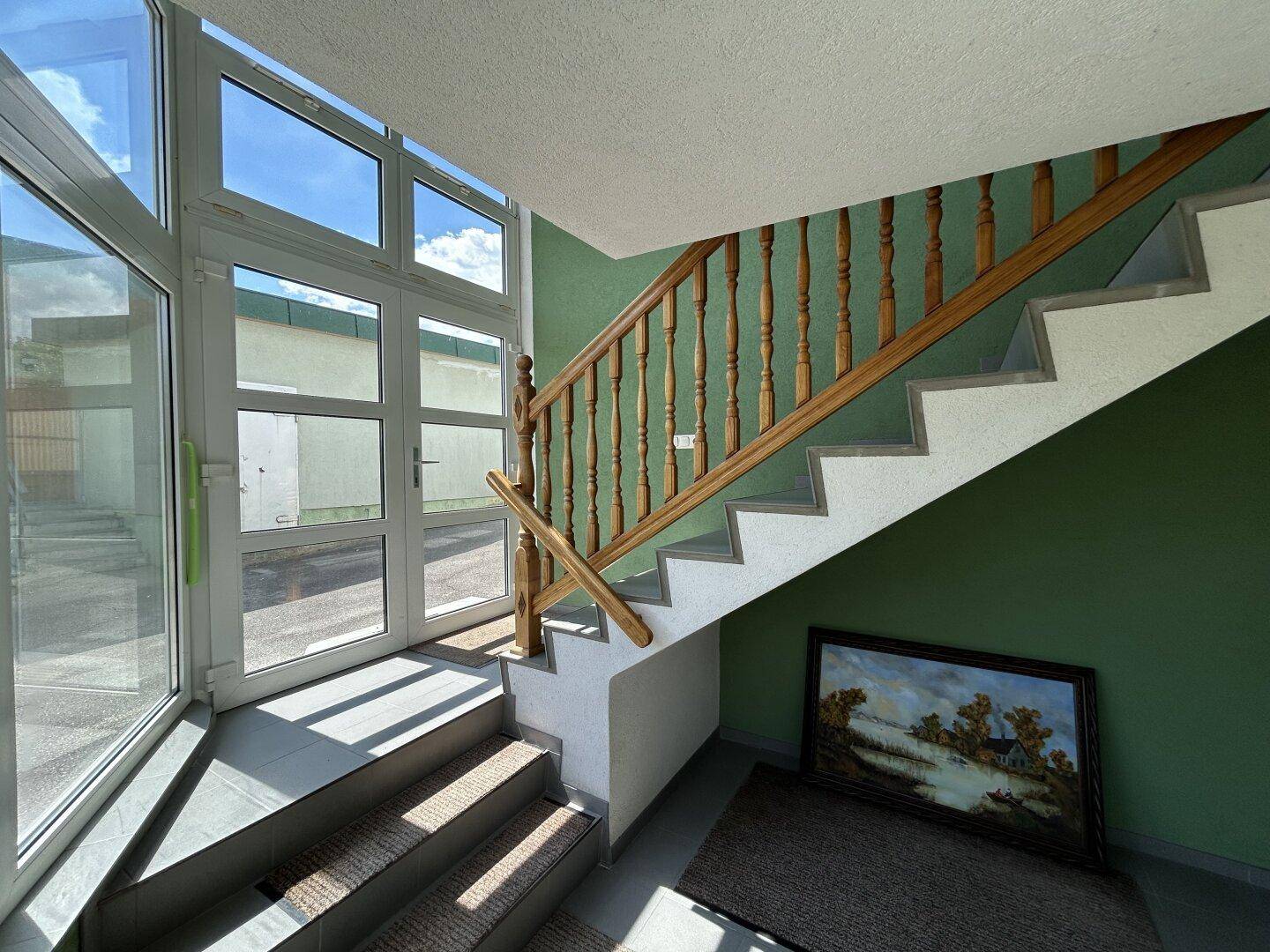 Eingangsbereich mit Treppe, Holzgeländer und großen Fenstern zum Außenbereich.
