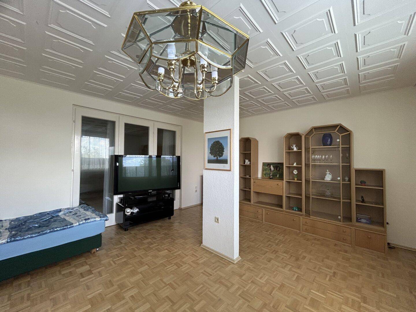 Geräumiges Wohnzimmer mit Parkettboden, Deckenpaneelen und großem TV-Bereich.