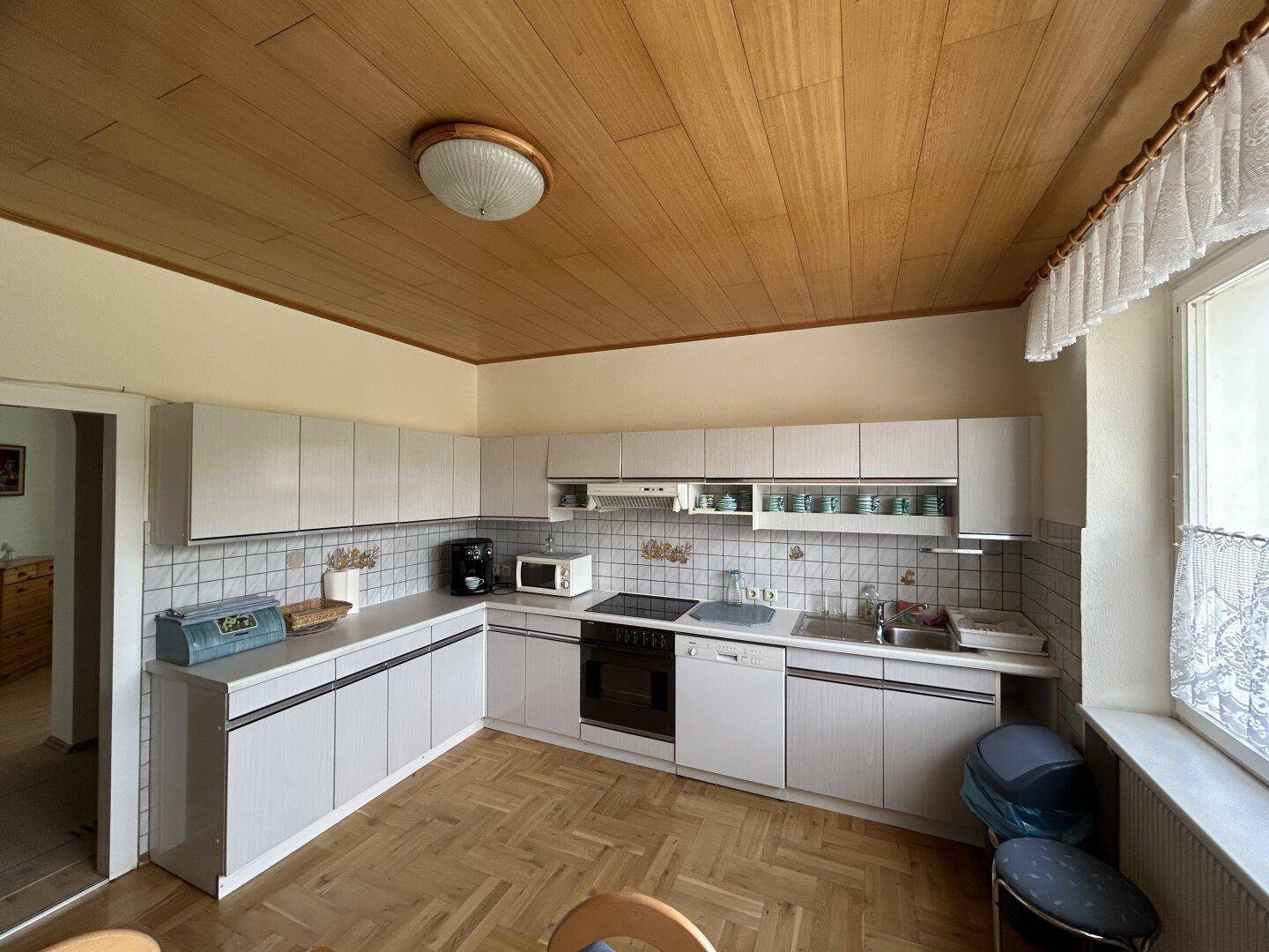 Funktionale Küche mit weißen Einbauschränken, Holzdecke und Fischgrätparkett.