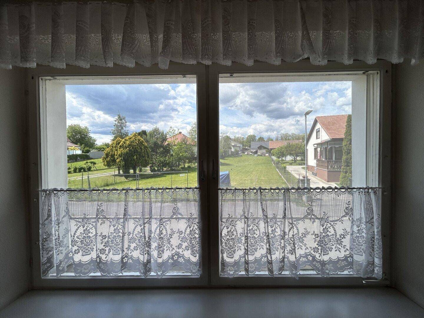 Blick aus dem Fenster auf den grünen Garten und die umliegende Wohngegend.