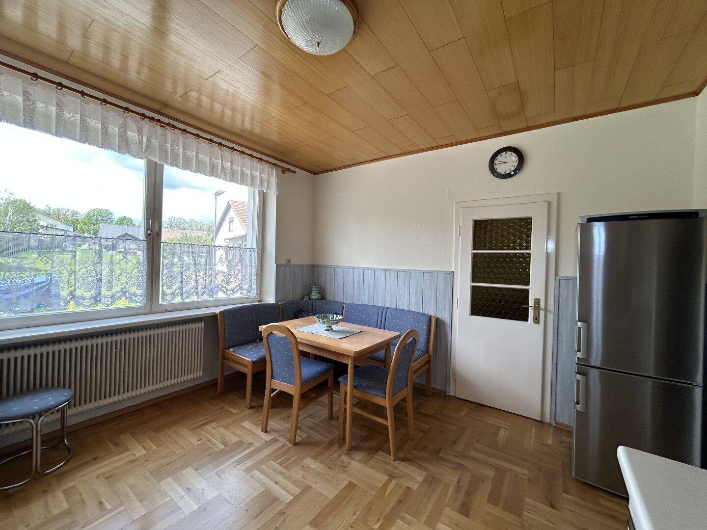 Gemütliche Wohnküche mit Essecke, Holzdecke und Blick ins Grüne.