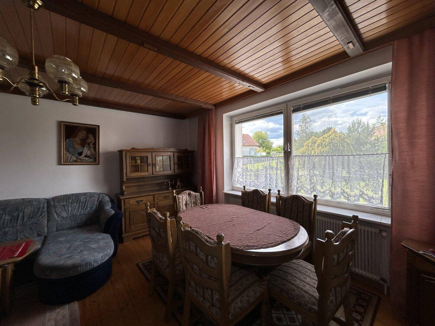 Traditionelles Esszimmer mit großem Holztisch, Sofa und Blick ins Grüne.