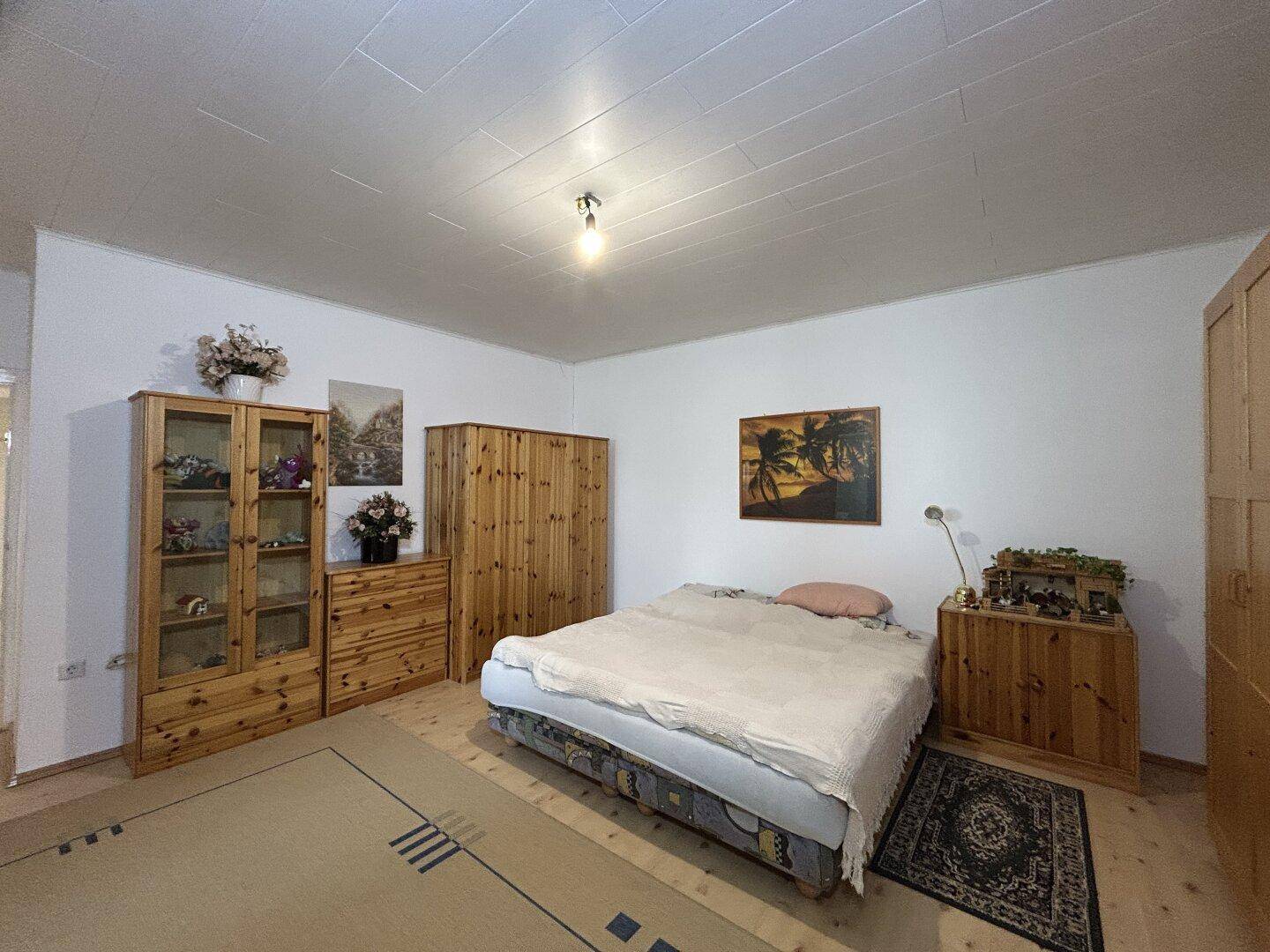 Geräumiges Schlafzimmer mit Doppelbett, Holzmöbeln und Teppich auf Parkettboden.