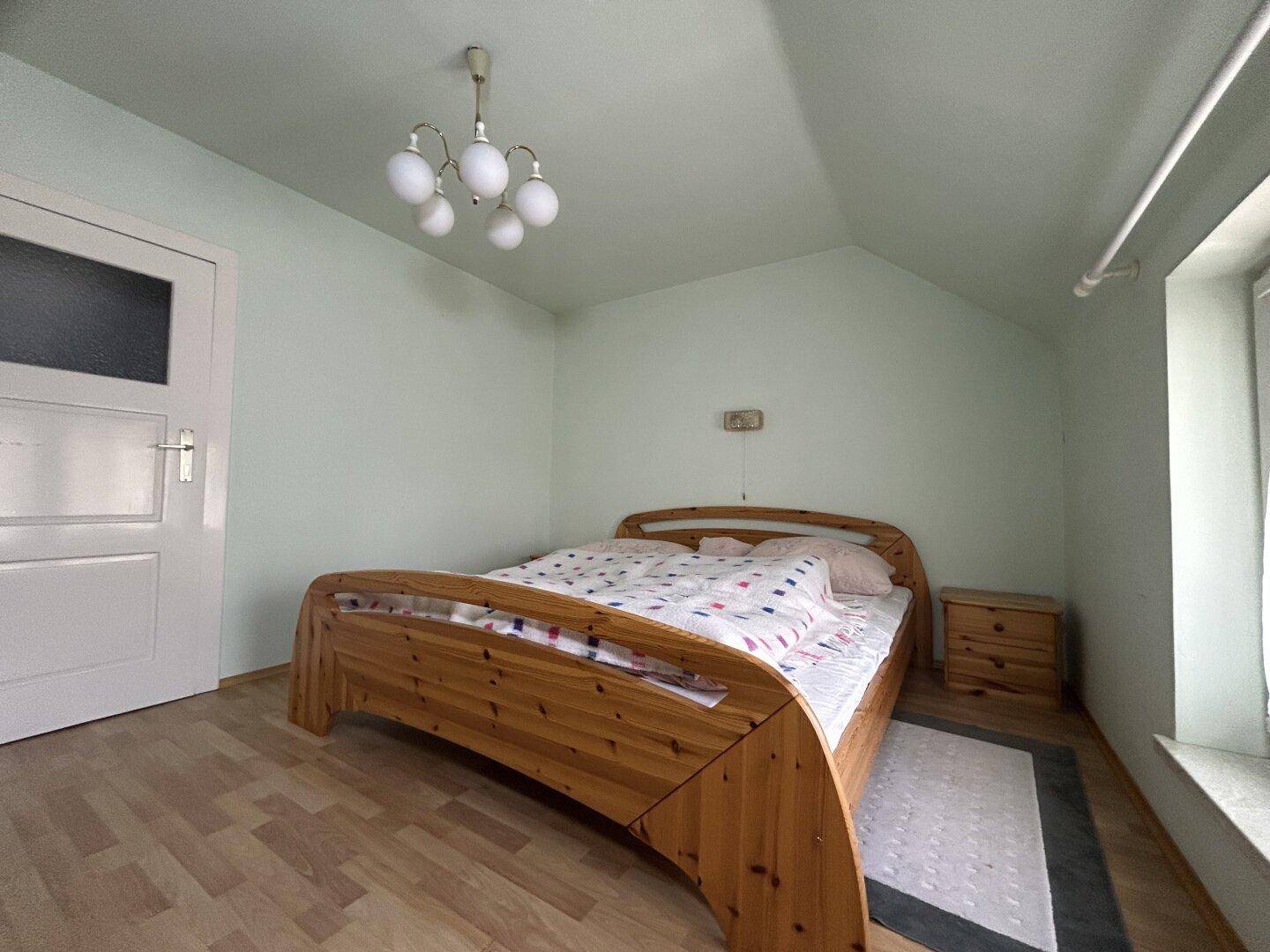 Gemütliches Schlafzimmer mit Holzbett, Dachschräge und Fenster mit Blick nach draußen.