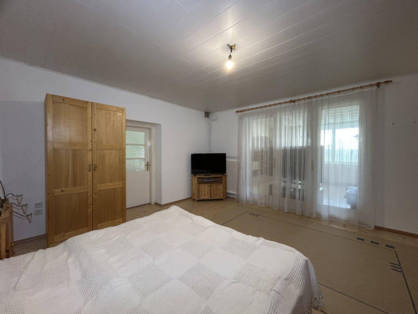 Schlafzimmer mit Doppelbett, Holzschrank und Zugang zu einem weiteren Raum.