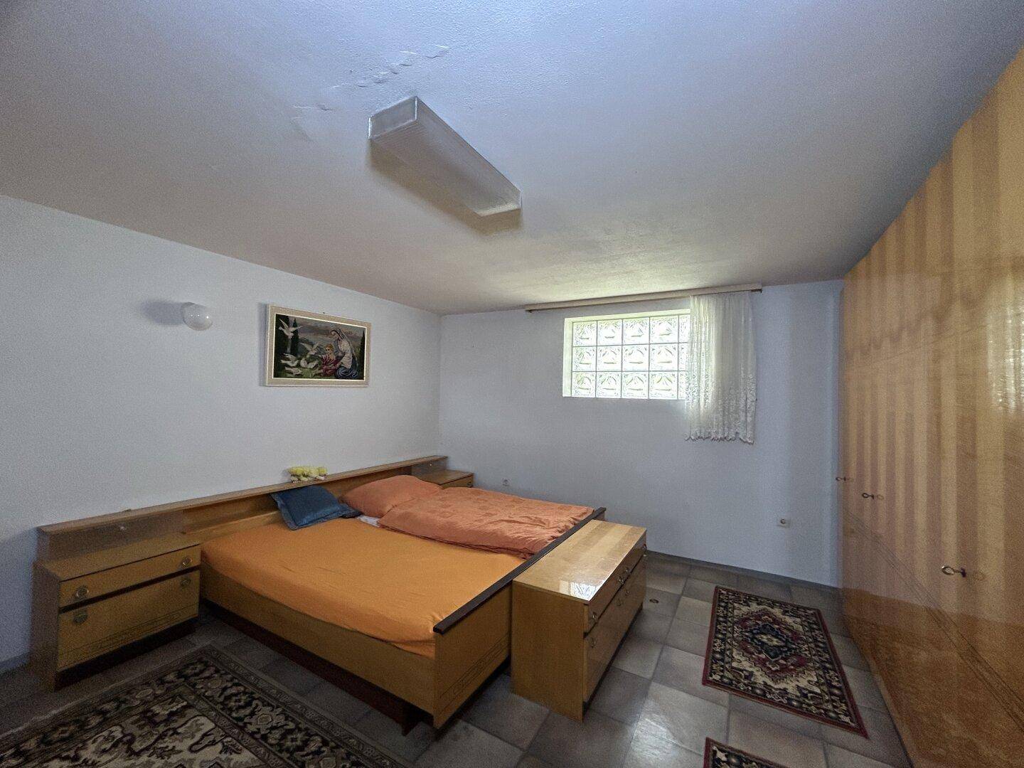 Schlafzimmer im Untergeschoss mit Doppelbett, Holzmöbeln und Glasbausteinfenster.