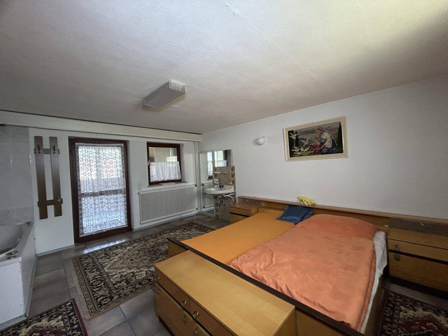 Schlafzimmer mit Doppelbett, integrierter Badewanne und Waschbecken, sowie Zugang nach draußen.