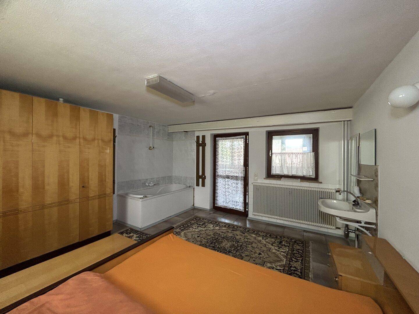 Geräumiges Schlafzimmer mit Holzschrank, Doppelbett und integrierter Badewanne im rustikalen Stil.