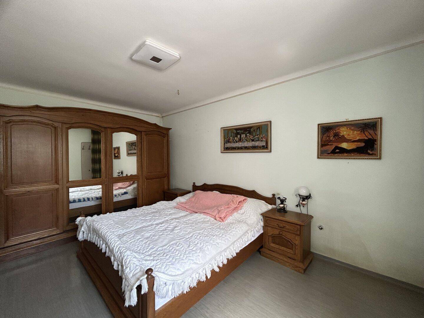 Schlafzimmer mit großem Holzschrank, Doppelbett und traditioneller Einrichtung.