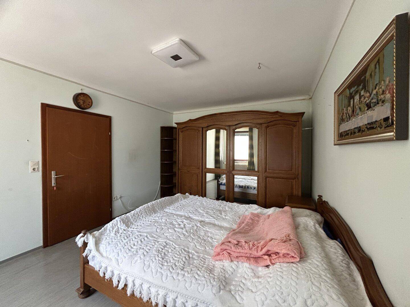 Geräumiges Schlafzimmer mit klassischem Holzschrank und Doppelbett in heller Farbgebung.