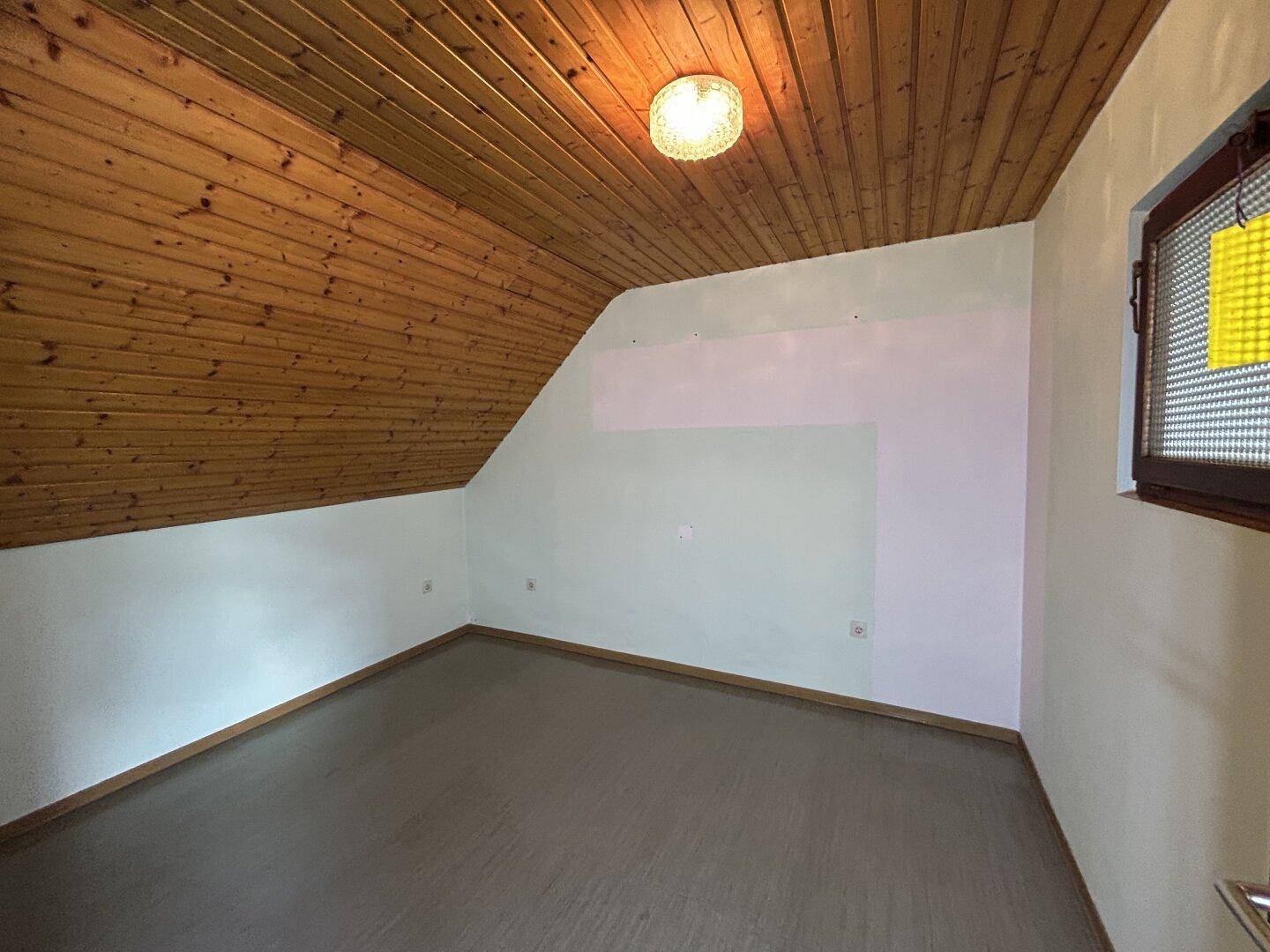 Leerer Dachbodenraum mit Holztäfelung an der Decke und schrägen Wänden.
