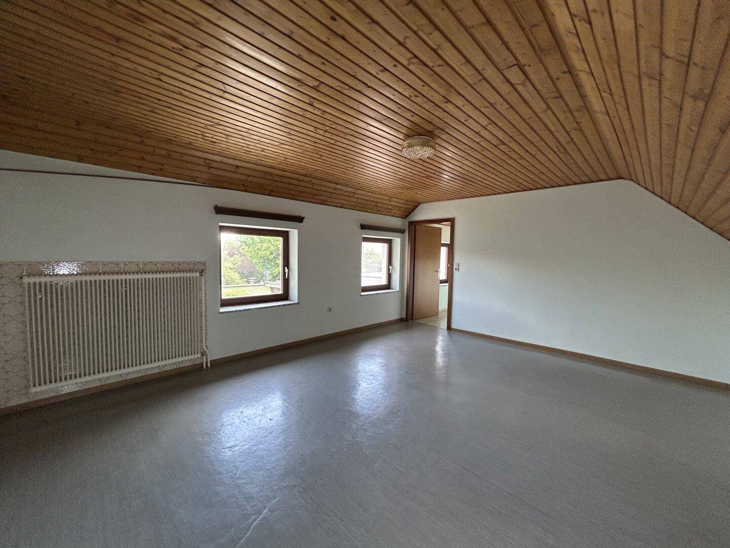 Geräumiger Dachbodenraum mit Holzdachschrägen, Fenstern und Blick ins Grüne.