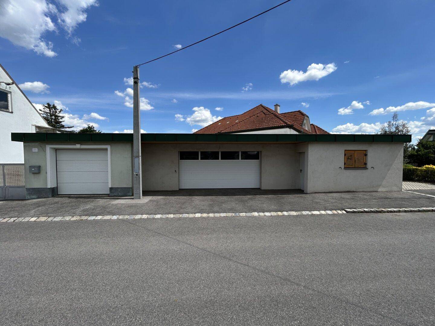 Nahaufnahme der Garagenfront mit zwei Rolltoren und einem Fenster zur Straße hin.