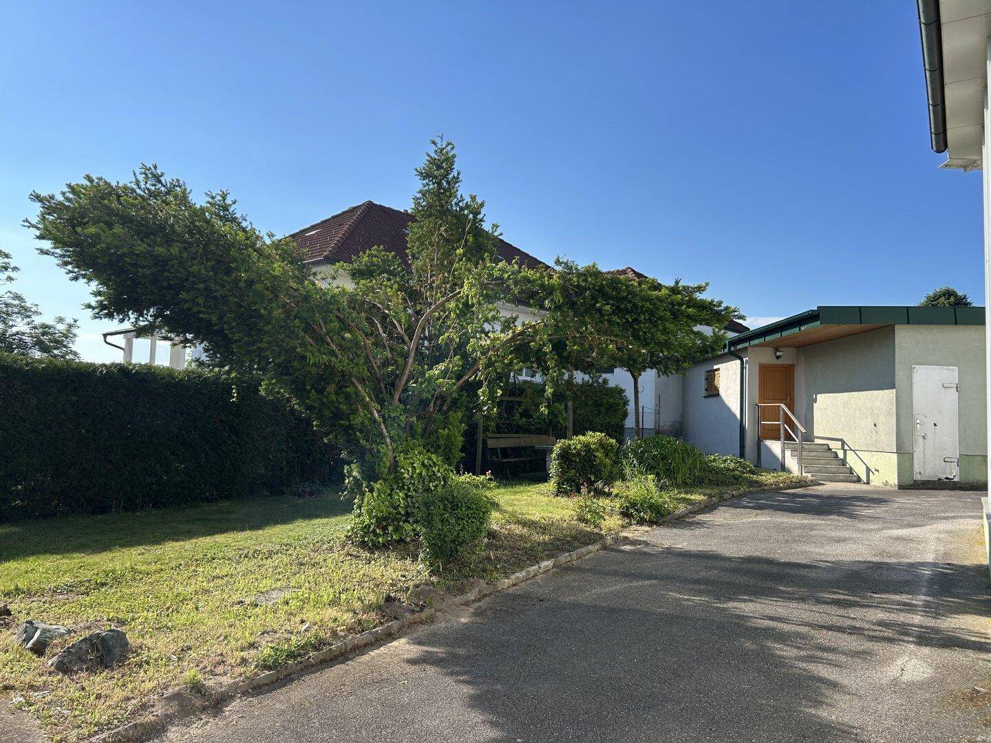 Außenansicht des Hauses mit Zufahrt und gepflegtem Vorgarten unter blauem Himmel.