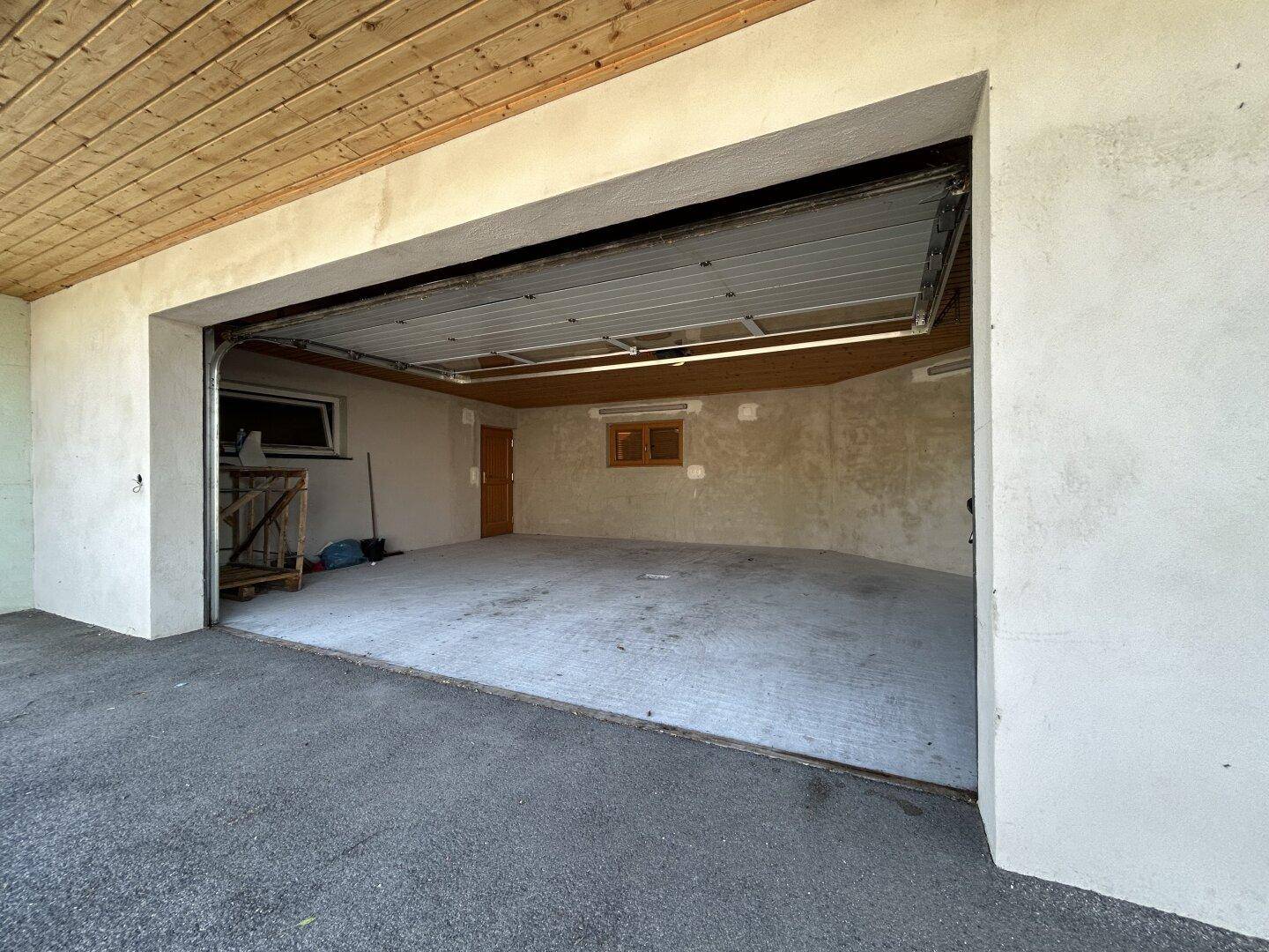 Geräumige Garage mit offenem Tor, Holzbalkendecke und ausreichend Platz für Fahrzeuge.