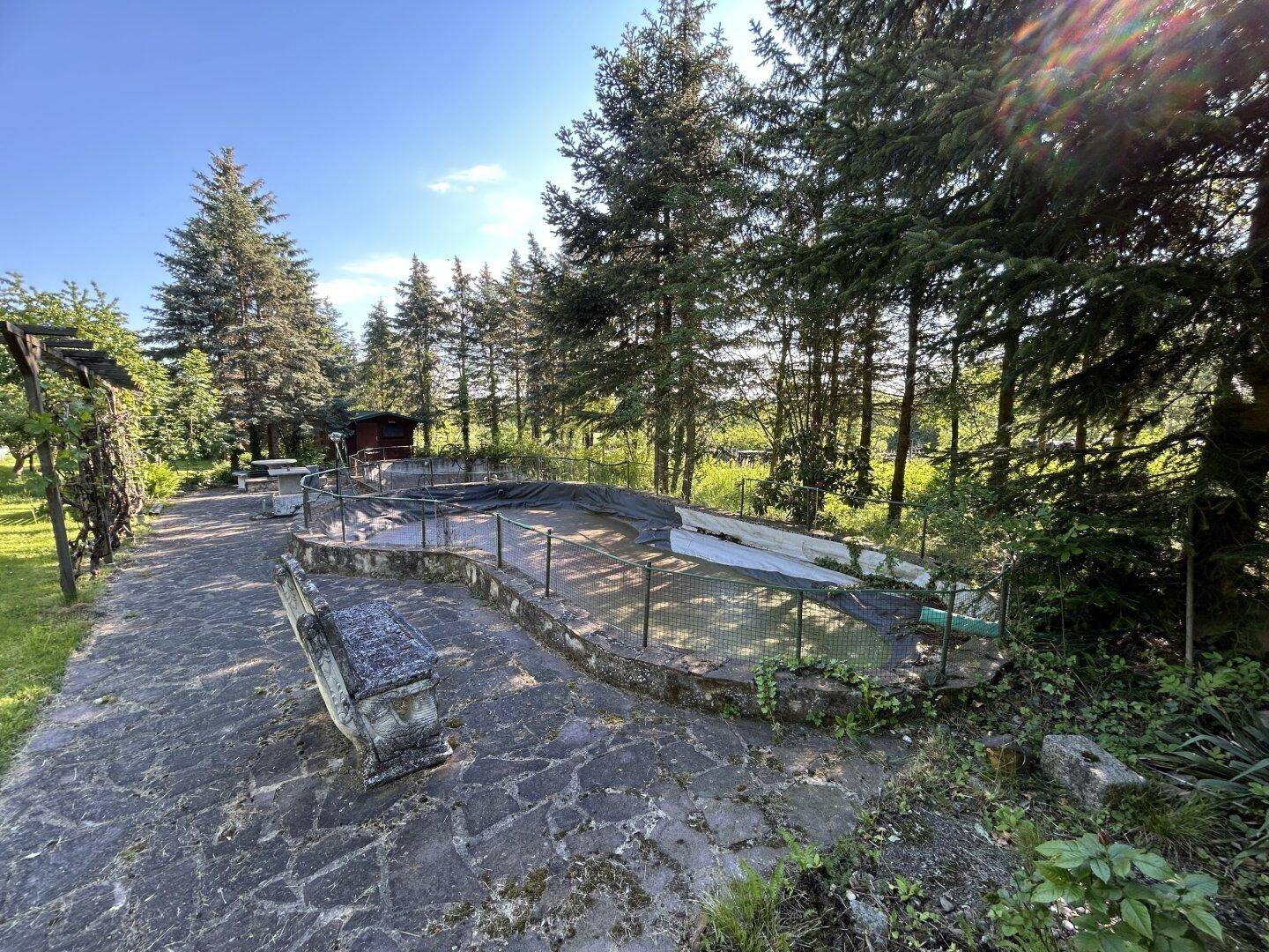Gepflasterter Gartenbereich mit großem, leeren Poolbecken und Sitzgelegenheiten.