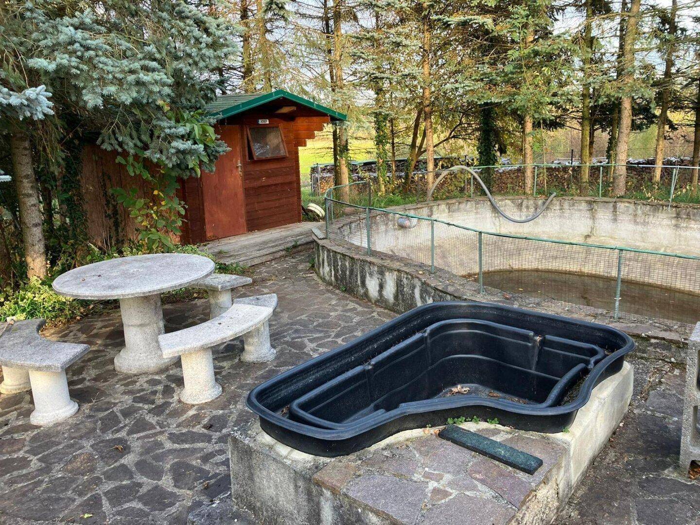 Gepflasterter Gartenbereich mit Steintisch, Bänken und einem kleinen Becken.