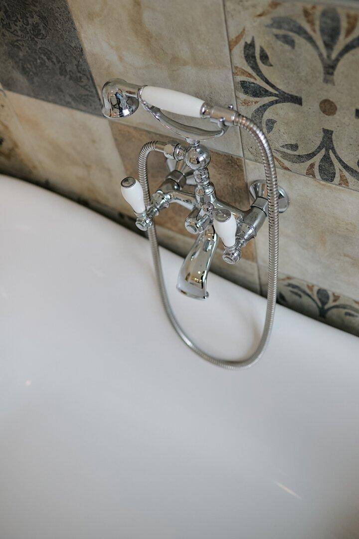Detailaufnahme einer klassischen Badewannenarmatur mit Handbrause an einer freistehenden Wanne.