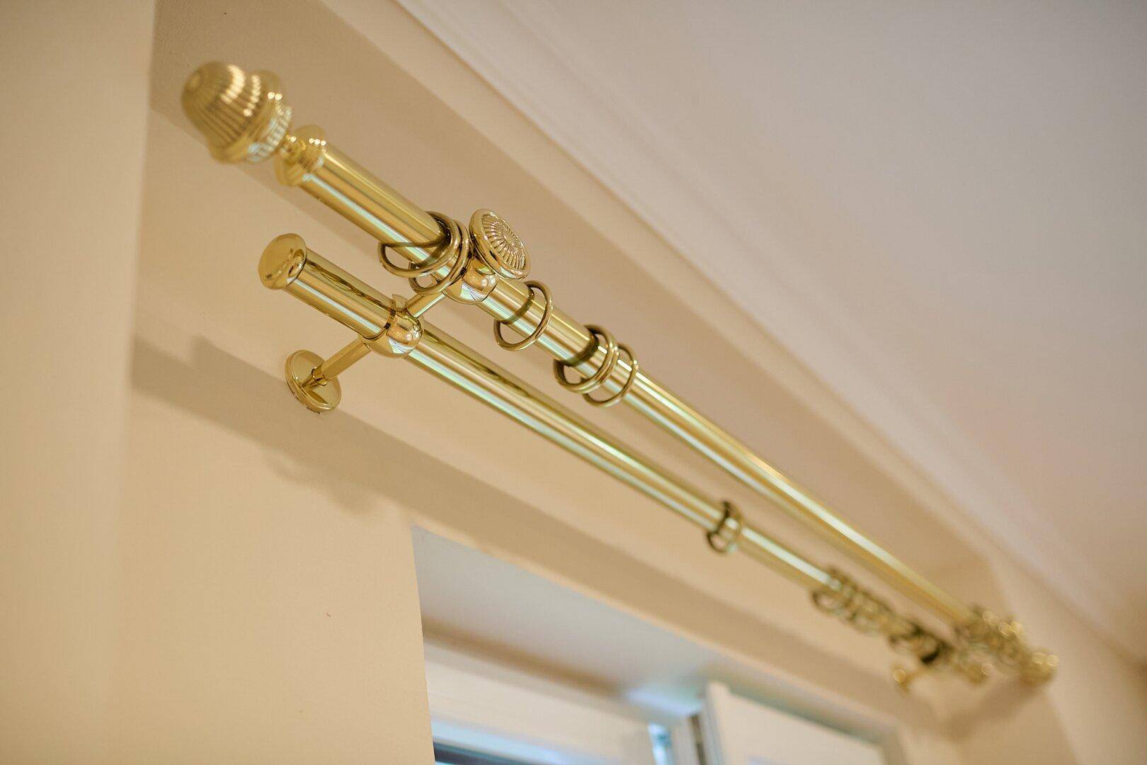 Detailaufnahme einer dekorativen, goldenen Gardinenstange über einem Fenster.