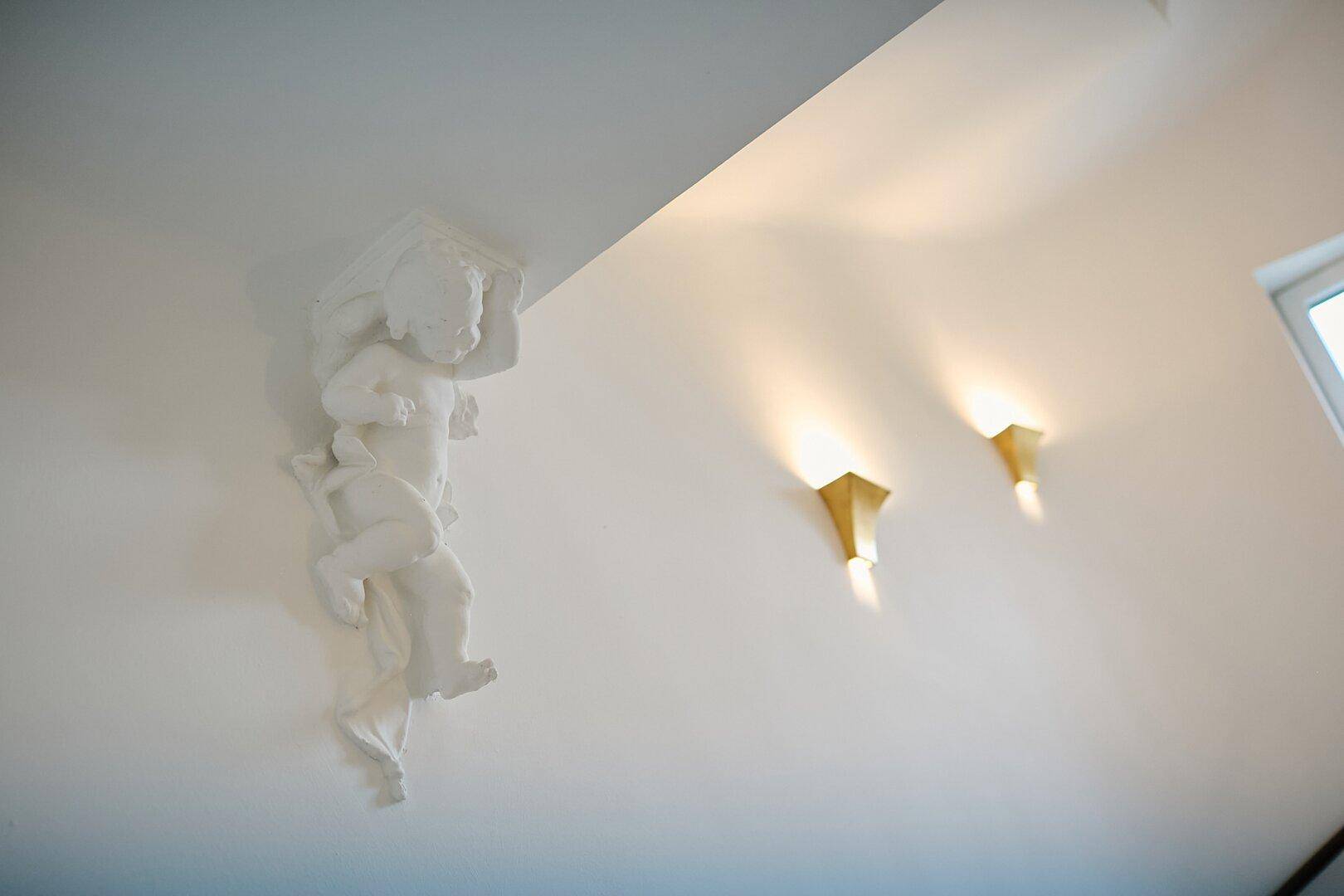 Dekorative Stuckfigur an der Wand mit indirekter Beleuchtung in einem hellen Innenraum.