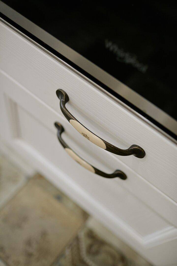 Nahaufnahme von eleganten Griffen an weißen Küchenschubladen mit traditionellem Design.