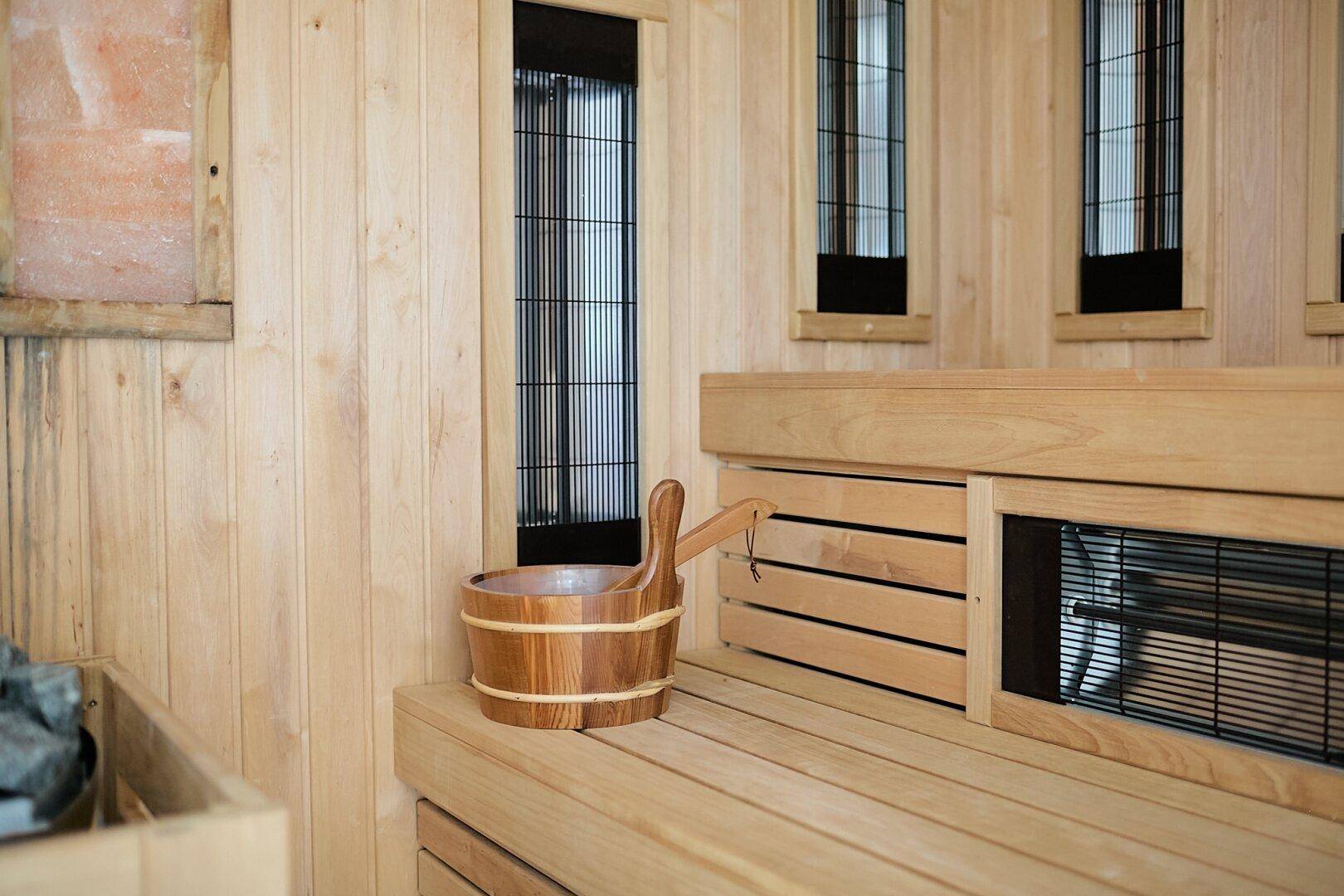 Innenansicht einer Holzsauna mit Bänken, Heizelementen und einem traditionellen Holzeimer.