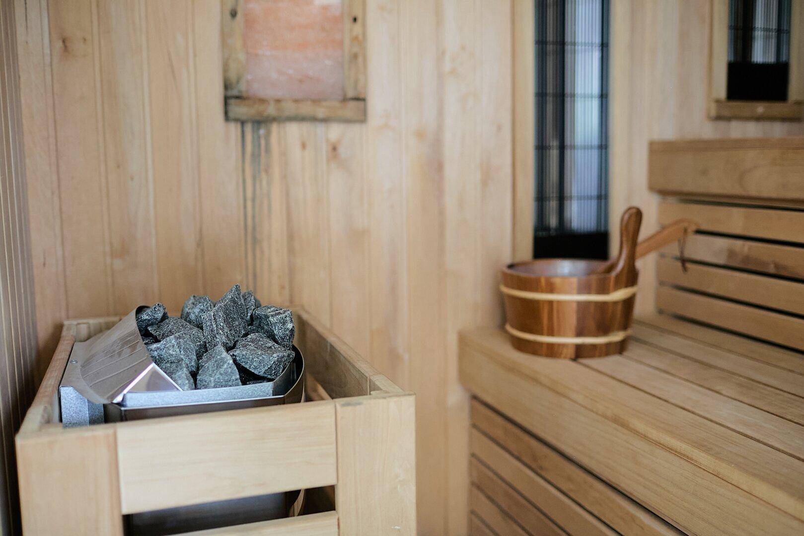 Innenansicht einer holzvertäfelten Sauna mit Sitzbänken und einem Saunaofen.