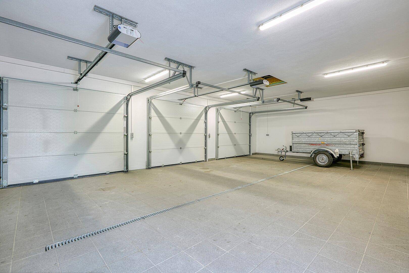 Geräumige Doppelgarage mit zwei Rolltoren, Betonboden und einem Anhänger.