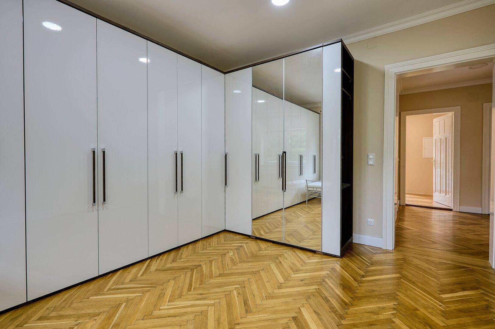 Raumecke mit Fischgrätparkett und einem großen weißen Einbauschrank mit Spiegelfront.