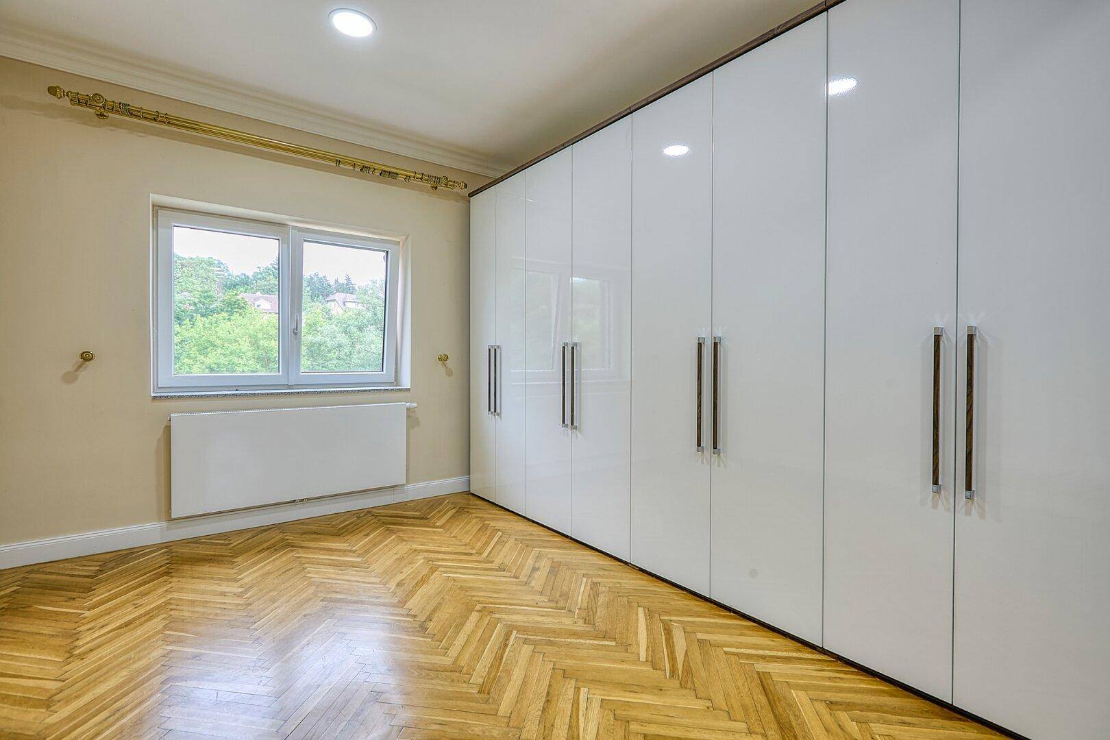Schlafzimmer mit Fischgrätparkett, beigen Wänden und einem großen weißen Einbauschrank.