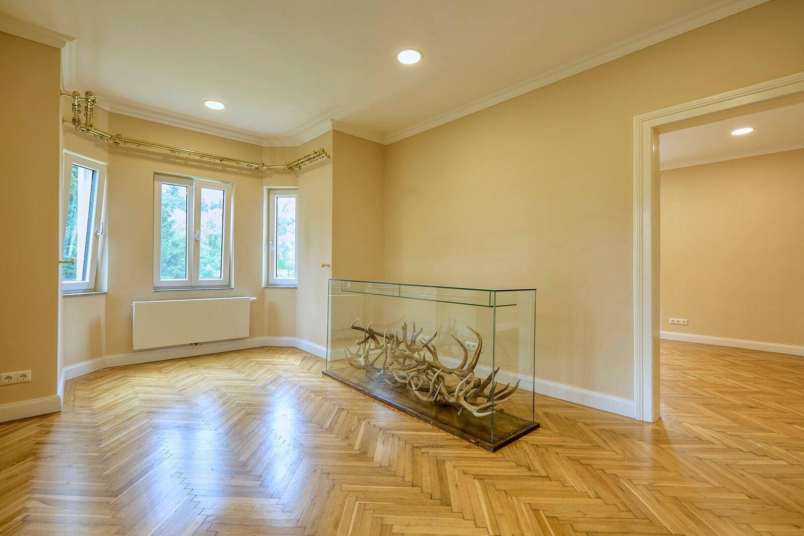 Heller Wohnbereich mit Fischgrätparkett, vielen Fenstern und einem dekorativen Geweih-Display.
