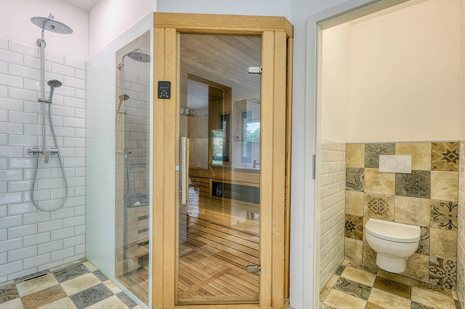 Badezimmer mit moderner Duschkabine, Holzkabinen-Sauna und separatem WC-Bereich.