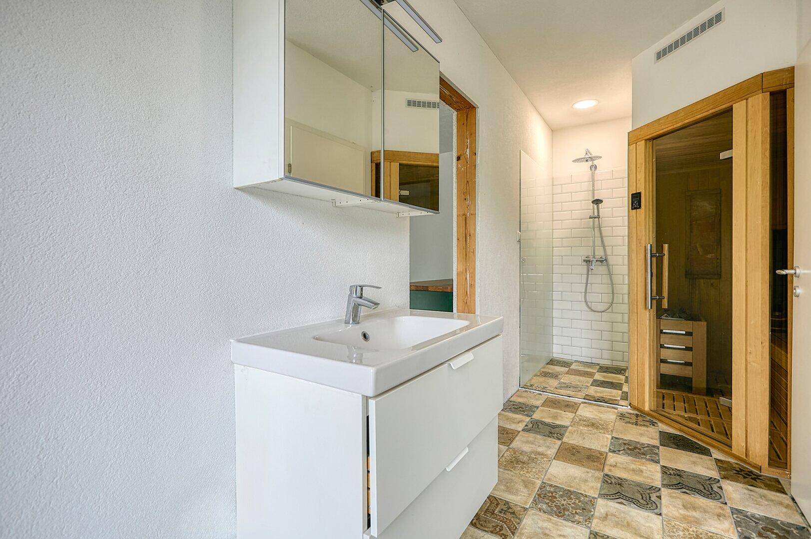 Modernes Badezimmer mit Waschbecken, Duschkabine und integrierter Sauna für Wellness.