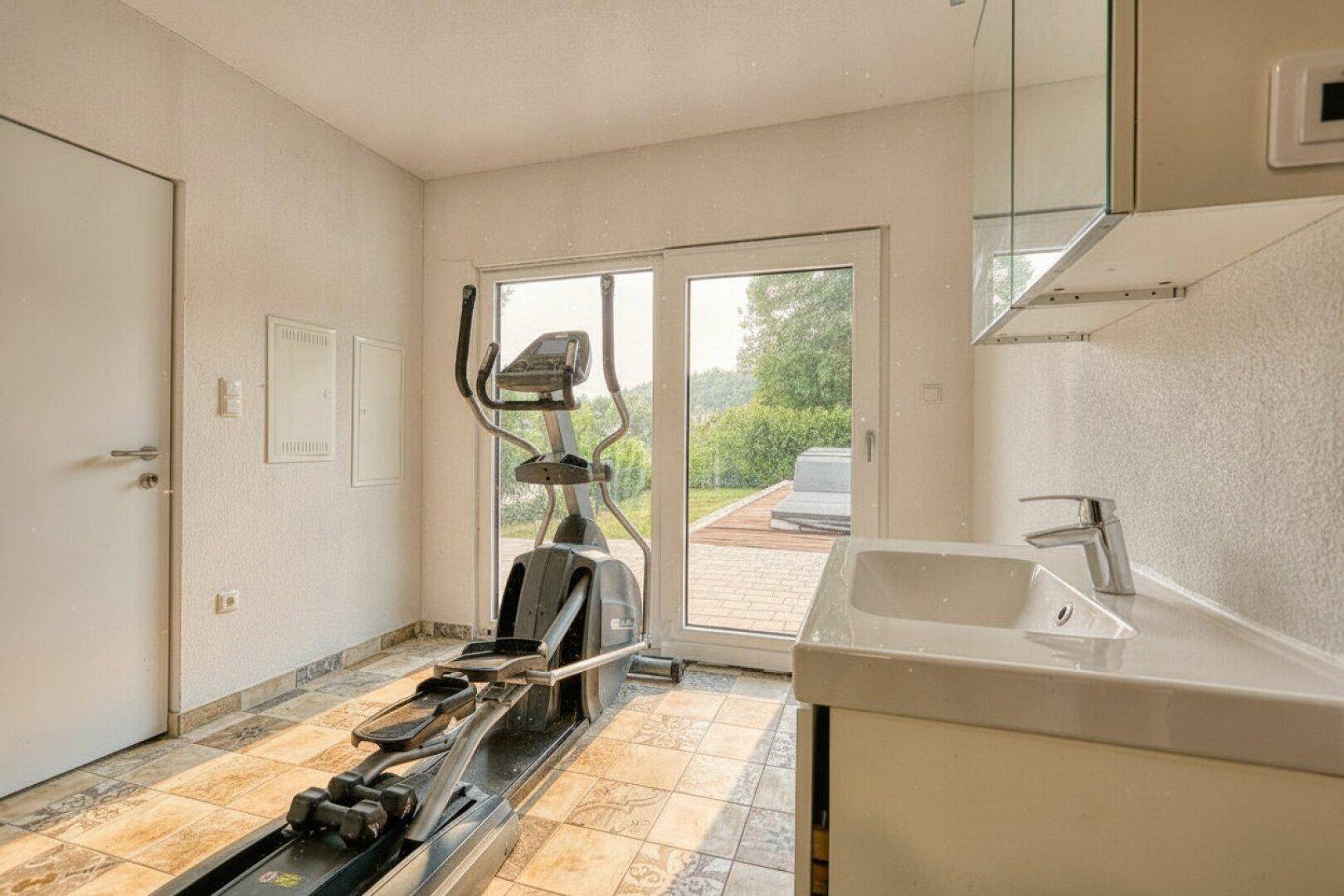Fitnessraum mit Trainingsgerät, Waschbecken und Zugang zu einem Außenbereich.