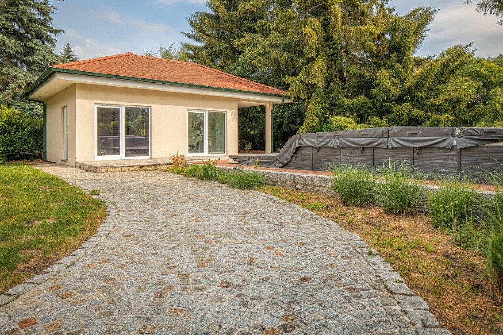 Außenansicht eines Hauses mit gepflasterter Auffahrt, Garten und einem Poolbereich.