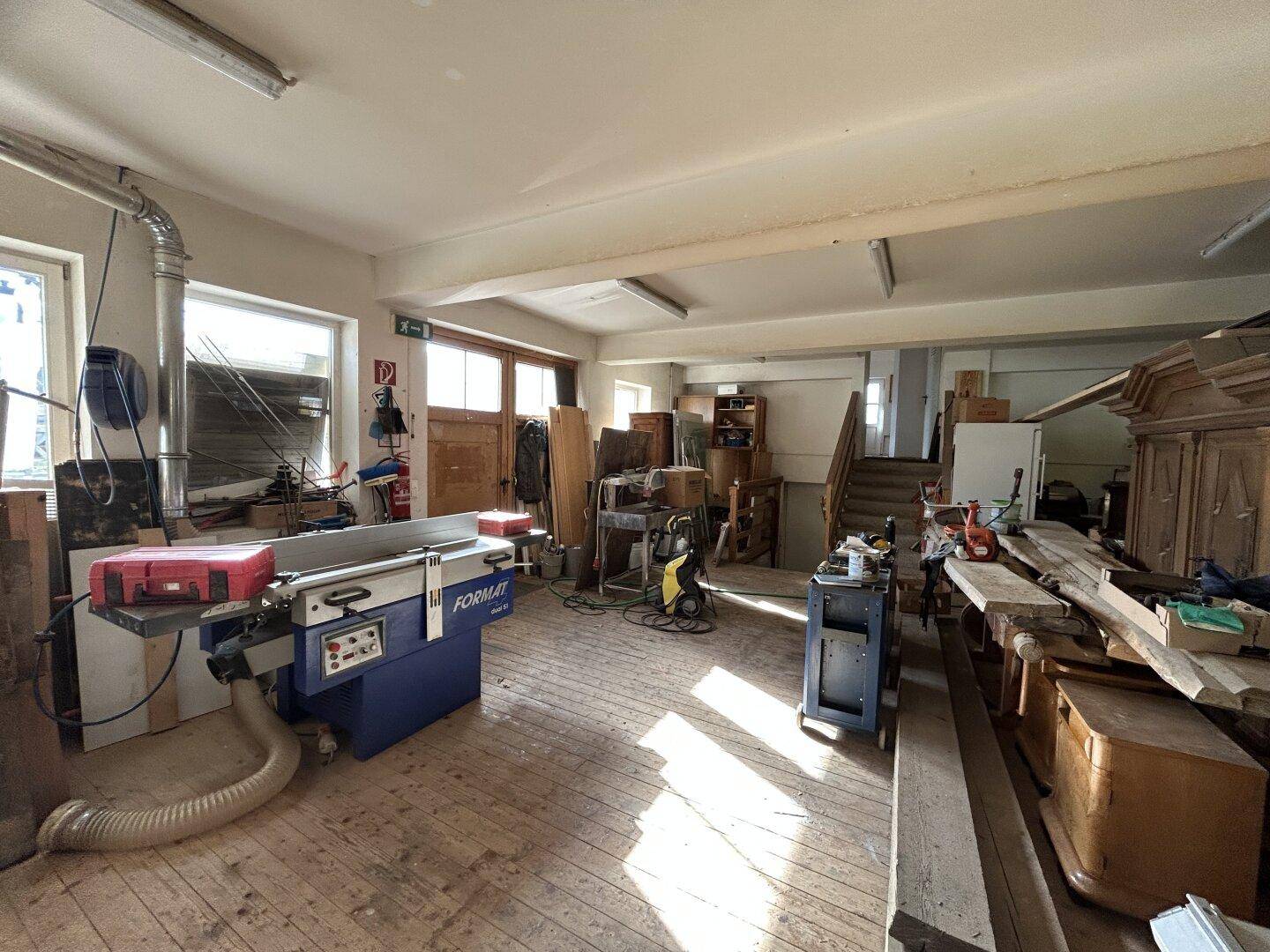 Werkstattraum mit großen Fenstern, Holzboden und verschiedenen Maschinen für die Holzbearbeitung.