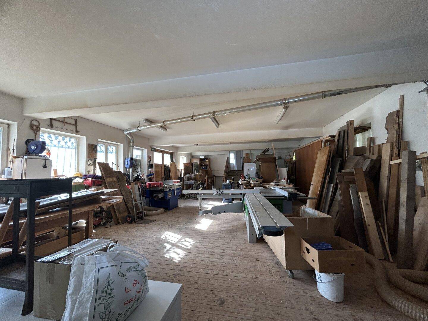Weitläufige Werkstatt mit Holzboden, vielen Fenstern und ausreichend Platz für Maschinen und Lagerung.