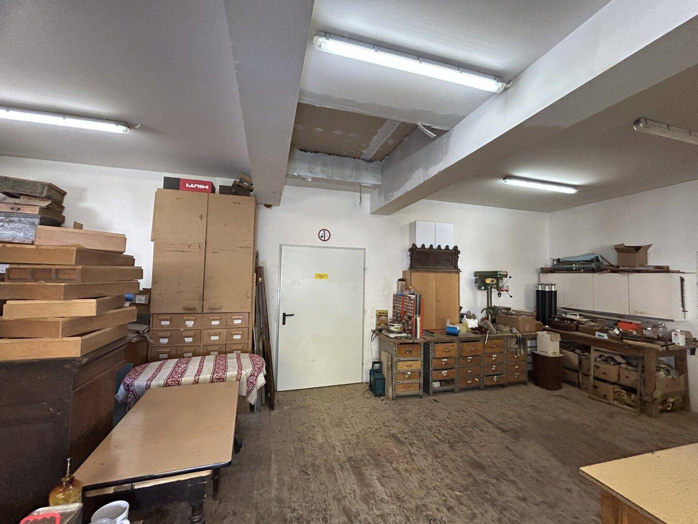 Geräumige Werkstatt mit Holzboden, Lagerflächen und guter Beleuchtung durch Leuchtstoffröhren.