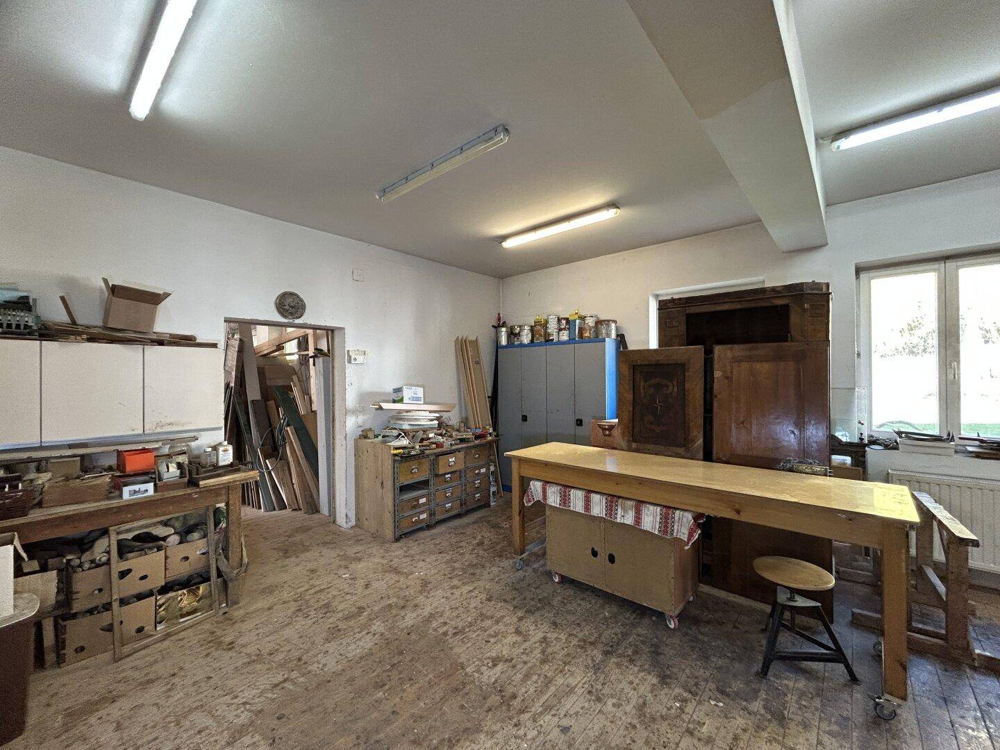 Werkstatt mit Holzboden, Arbeitsbereichen und Fenstern, die Tageslicht hereinlassen.