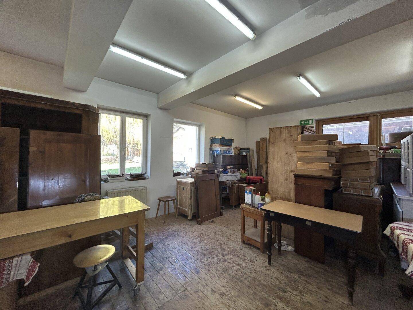 Helle Werkstatt mit Holzboden, Fenstern und verschiedenen Arbeitsstationen für handwerkliche Arbeiten.