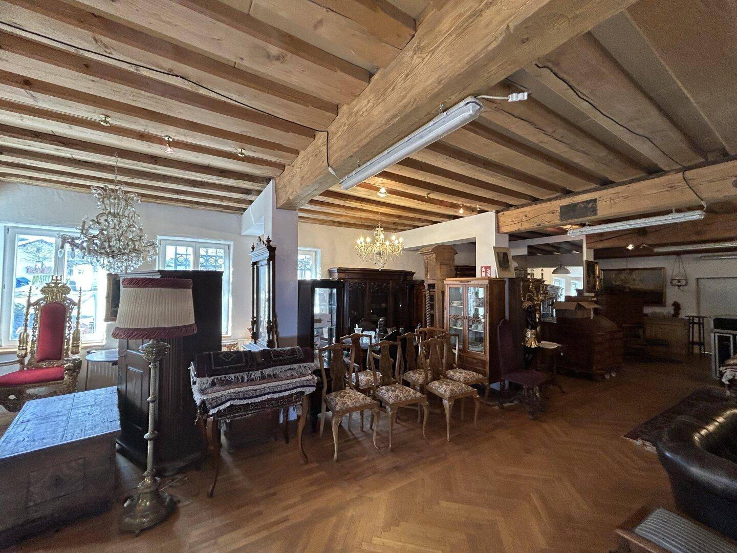Großer Ausstellungsraum mit Holzbalkendecke, Fischgrätparkett und antiken Möbeln.